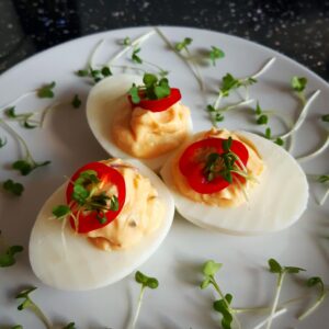 a picture of deviled eggs served on a plate with red chili and cress garnish
