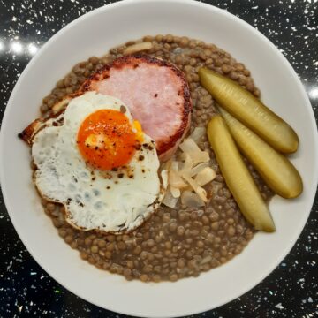 Lentil stew in a bowl, served with gammon, fried egg and gherkins.