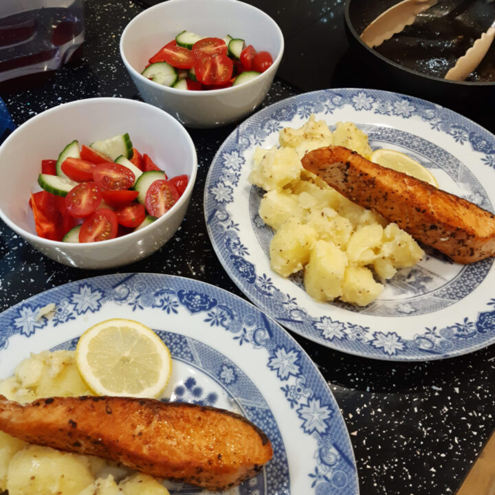 a picture of two plates with salmon fillets, boiled potatoes and salad bowls