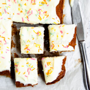 picture of carrot cake traybake with light cream cheese frosting and colorful sprinkles cut into squares