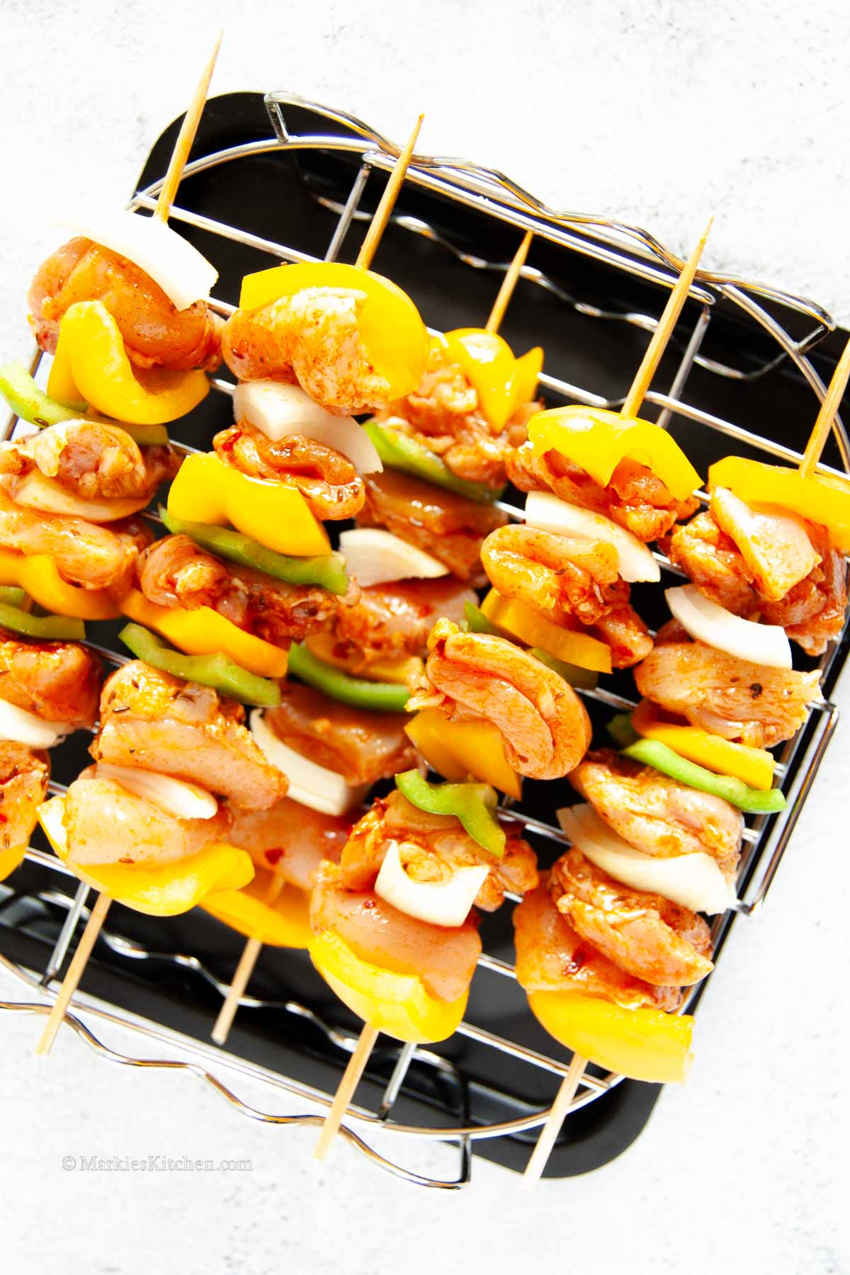 A top down photo of uncooked chicken kebabs with peppers and onion, stacked on a grill, ready to go in an air fryer.