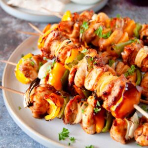 A square photo of a plate with stacked chicken kabobs, sprinkled with fresh chopped parsley.
