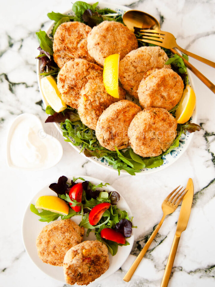 tuna and potato fish cakes erved on a plate with salad and lemon wedges
