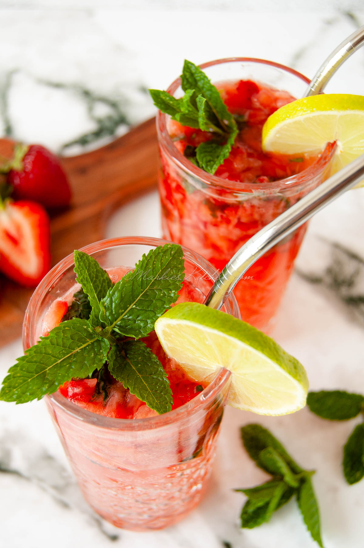 a close up photo of two glasses with strawberry and lime mojito, decorated with fresh mint