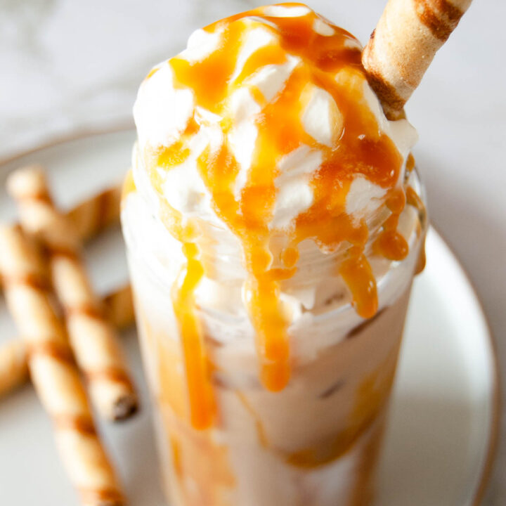 A photo of caramel iced latte with whipped cream, toffee sauce and waffle served in a tall glass.
