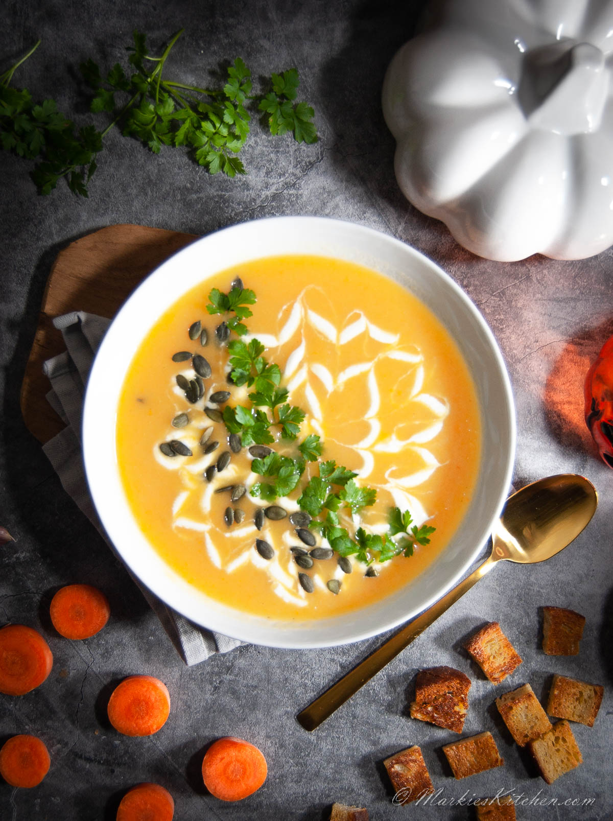A top-down photo of a plate with pumpkin soup, decorated with fresh cream, and sprinkled with seeds and chopped herbs.