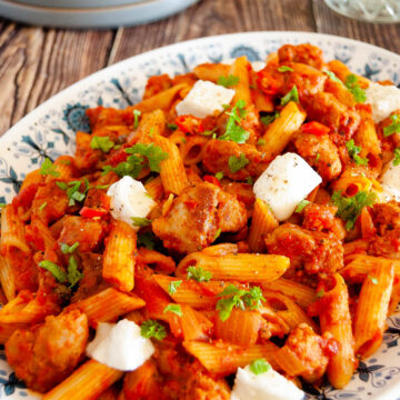 A photo of a large plate with pasta with tomato sauce and meat chunks.