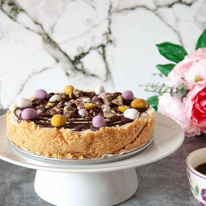A photo of a cheesecake with Easter chocolate eggs on a cake stand.