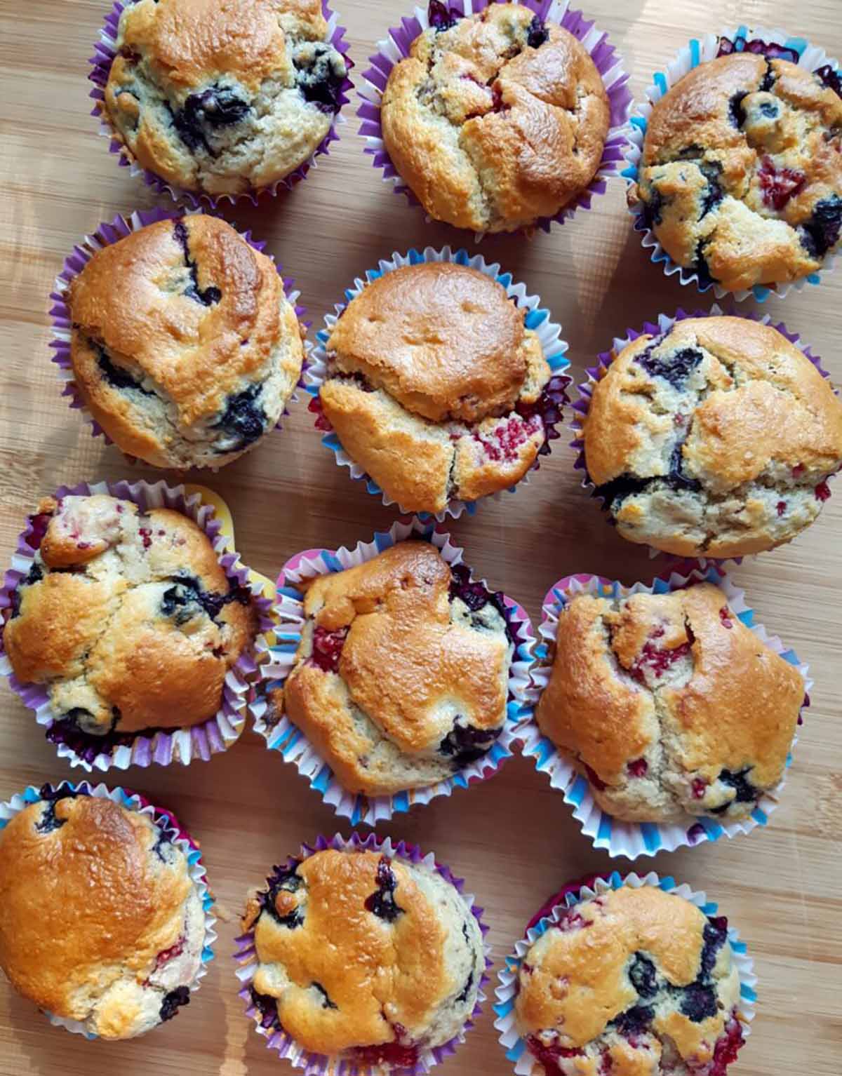 A top down photo of twelve oat muffins with fruit in paper cups.
