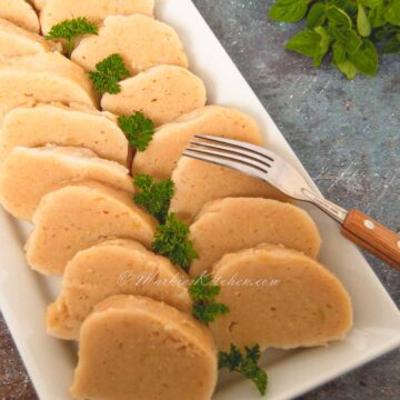 A photo of a plate full of sliced potato dumplings, garnished with fresh parsley.