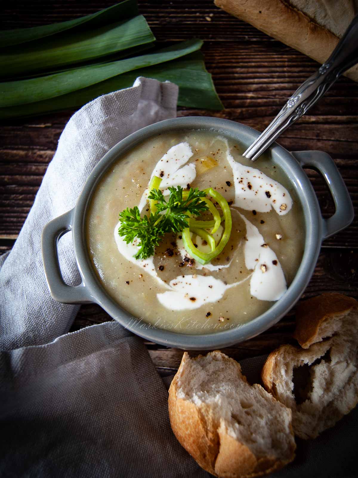 A photo of a bowl of soup with cream, and herbs on top, served with a rustic baguette.