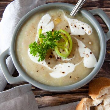 A photo of a leek and potato soup served with cream, chopped herbs and crusty bread.