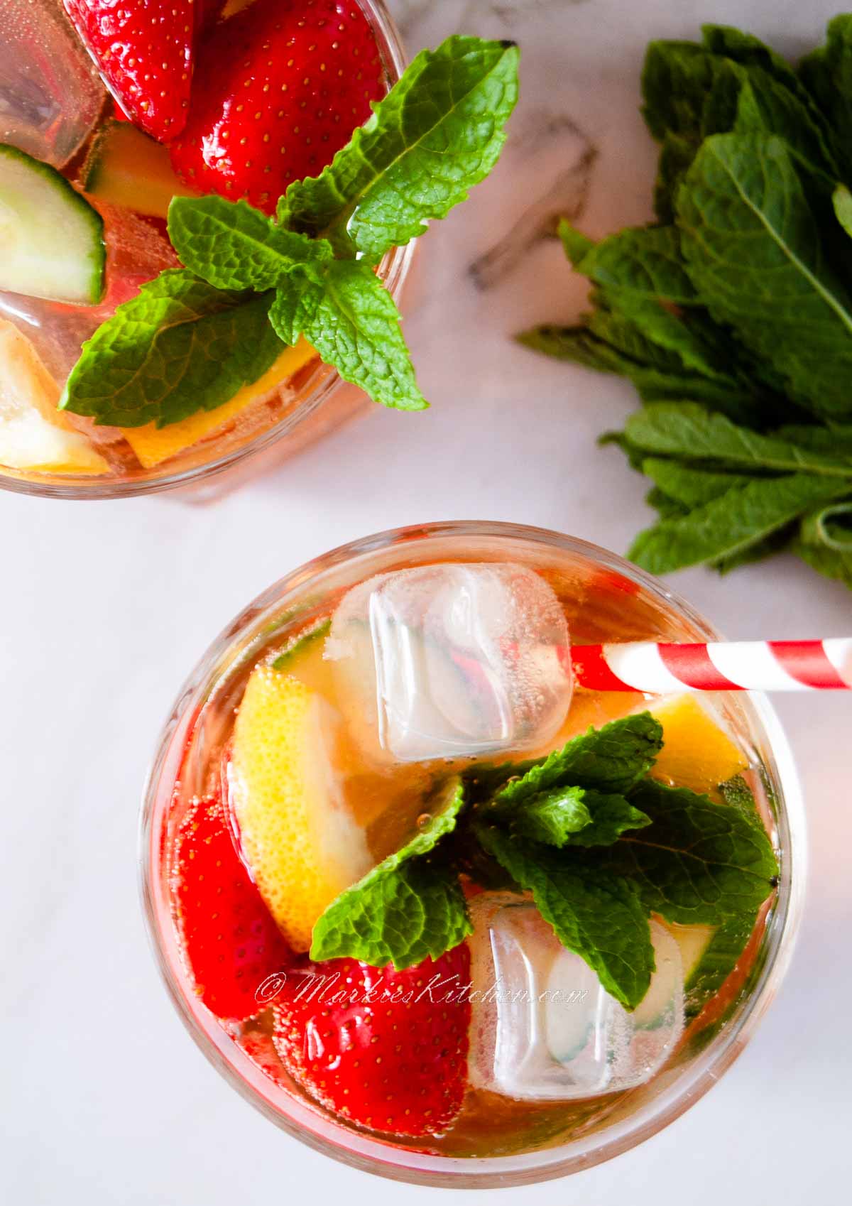 A top down photo of two glasses of non-alcoholic Pimm's, garnished with sliced strawberries, lemons, cucumber, and fresh mint leaves.
