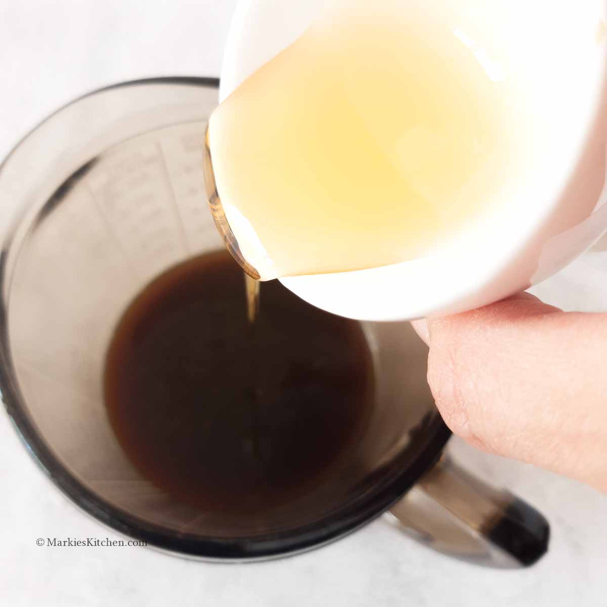 A photo of a hand pouring a yellow syrup to a jug with coffee.