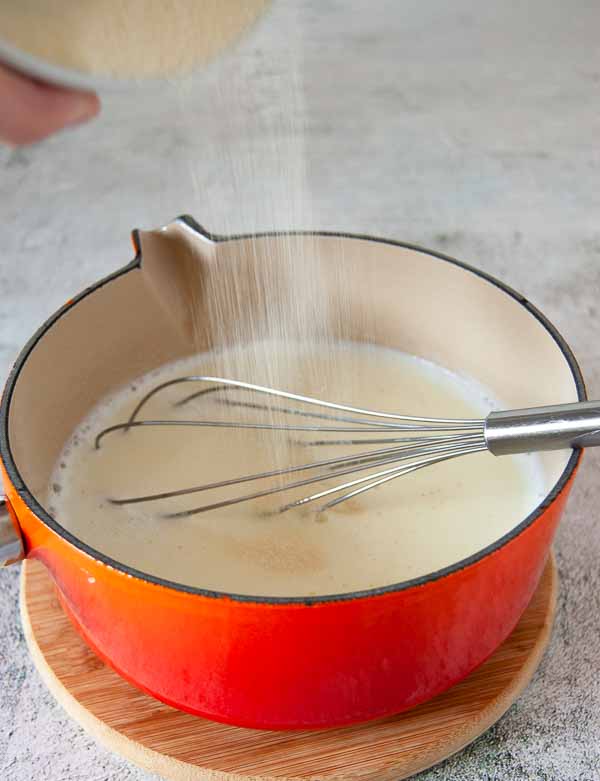 A photo showing semolina flour being added to a saucepan with hot milk.