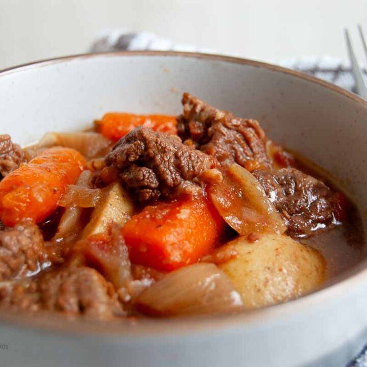 A bowl with cooked beef, carrots, potatoes and onion in a sauce.