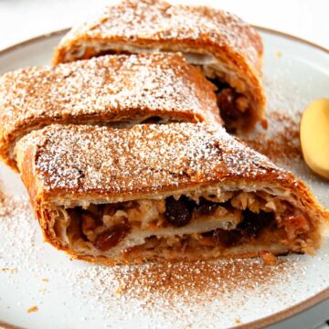 A close-up photo of three slices of apple strudel dusted with icing sugar and cinnamon powder.